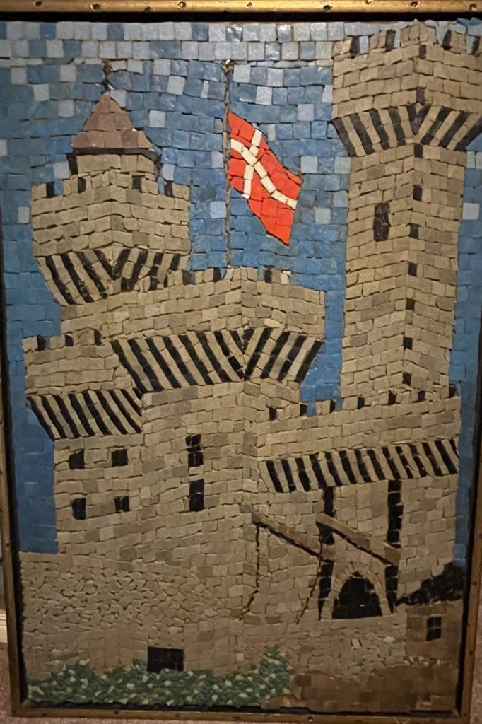 Mosaic of a grey castle against a blue sky, flying a red flag with a white cross.