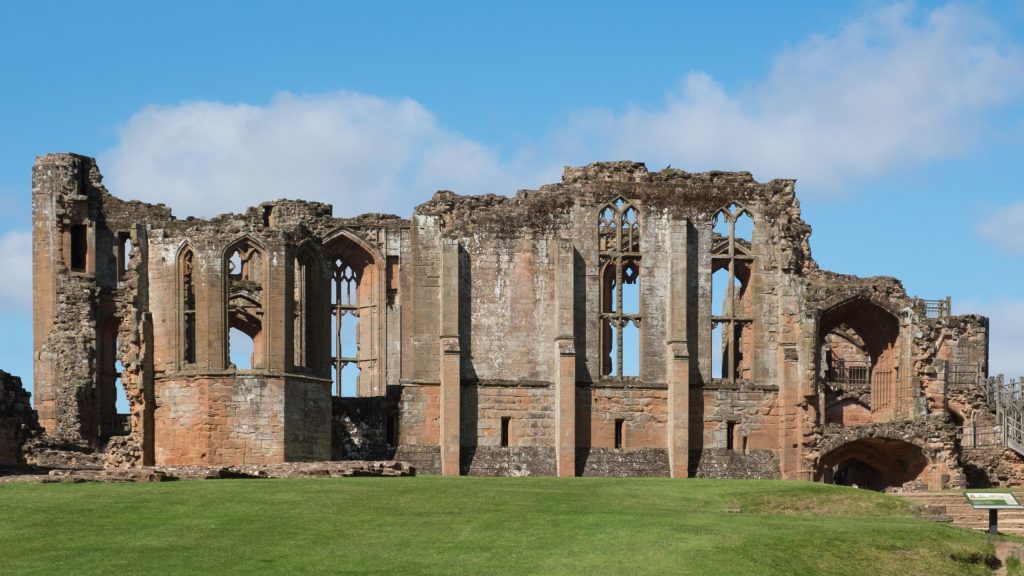 Photograph of the ruins of John of Gaunt’s Great Hall at Kenilworth Castle, in brown stone with lacy, pointed windows.