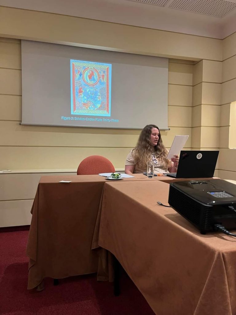 Person presenting at a table with a projected image labeled "Figure 2: Scivias-Codex Plate Thirty-Three" on the screen.