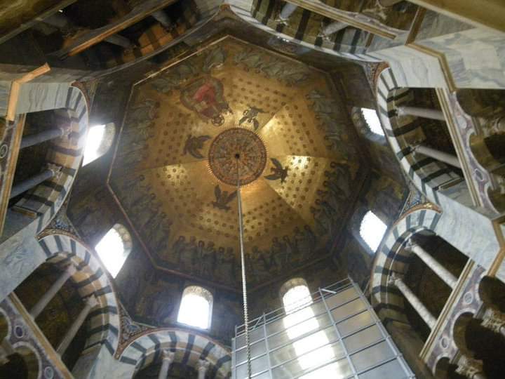 Interior view of an octagonal dome with golden mosaics and scaffolding below.