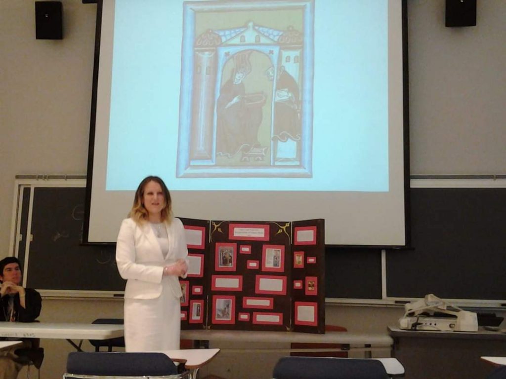 Person in white suit presenting in a classroom with a projection and display board.