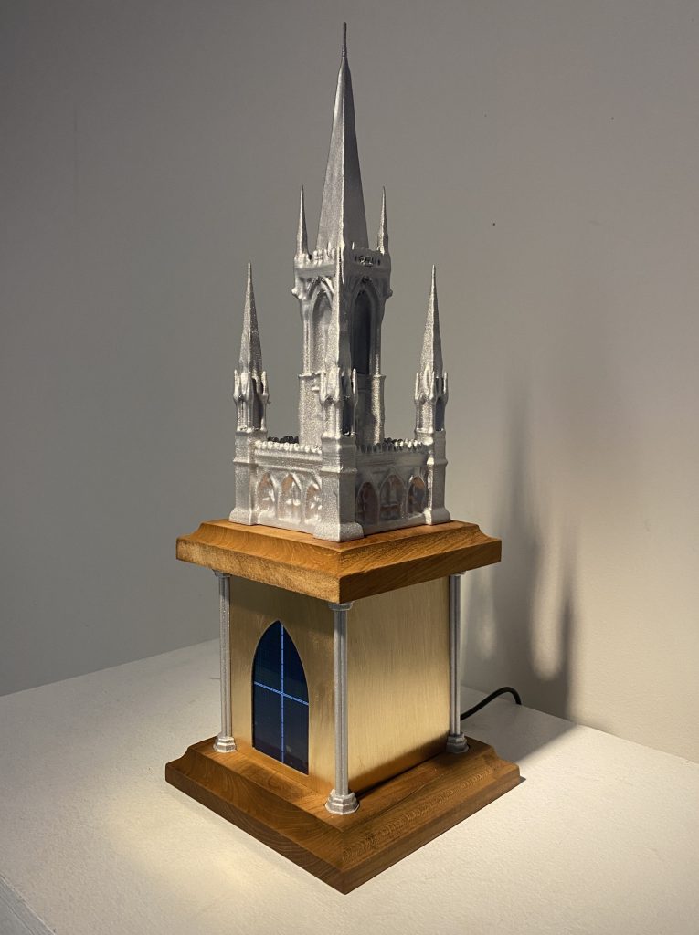 A small replica of a medieval church with tall spiky towers made of a silver metal material with a wooden base resting on a table.