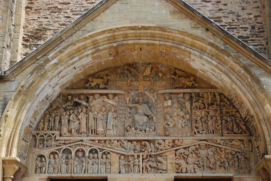 Stone tympanum showing three registers filled with many figures. At the center, Christ is enthroned.