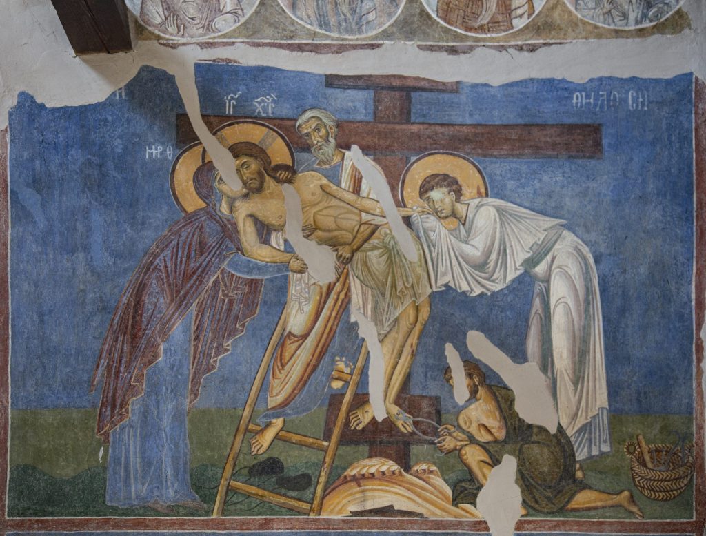 Painted wall depicting four figures lowering the fifth off of a cross. There is notable damage to the surface.