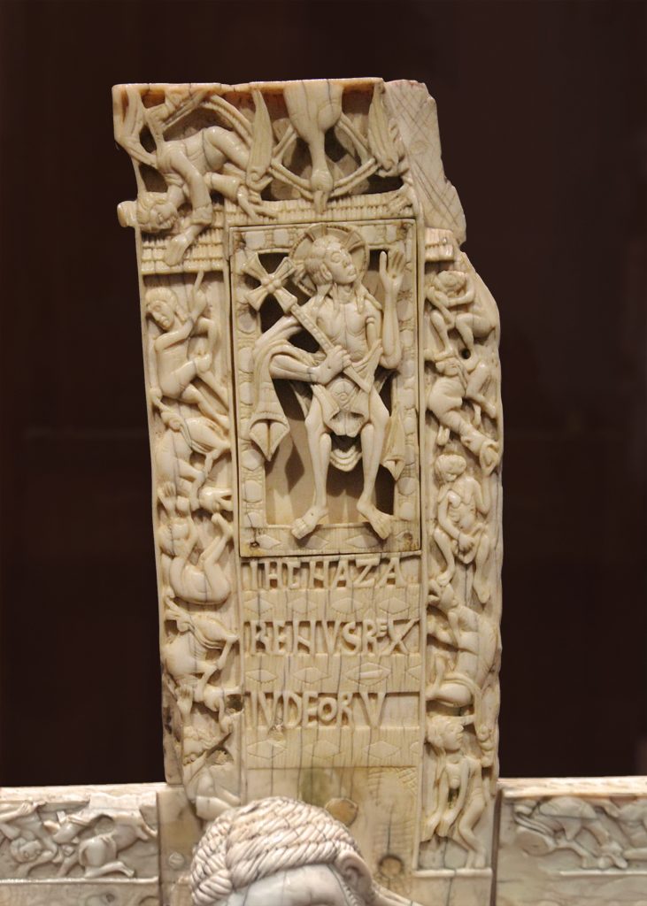 Man with a cross behind his head and a cross staff stands among various naked bodies and Latin text.