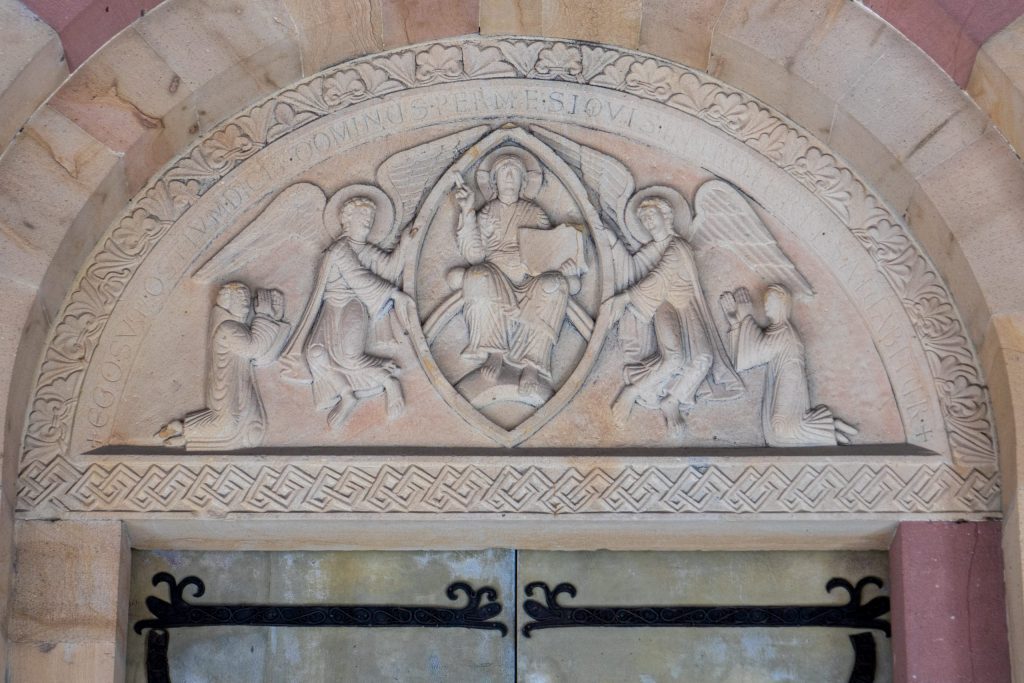 Man and woman kneel at either side of two angels holding a seating figure between them. An inscription runs along the top edge.