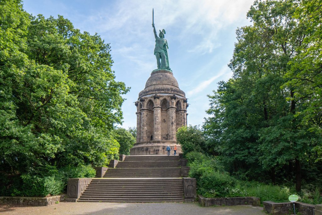 Giant copper statue of a man holding a sword aloft sits on top of a stone tower.