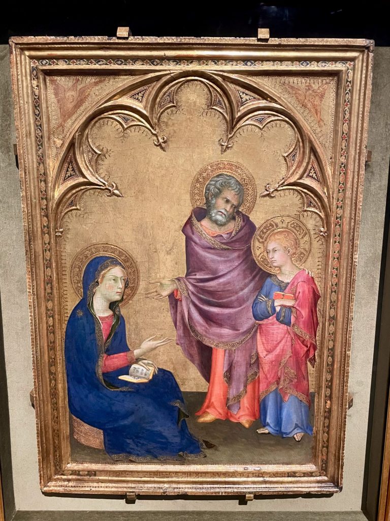 A painting of a seated woman in a blue cloak, a standing bearded man in a lavender cloak, and a standing child wearing a blue undergarment and a red cloak and holding a book. The painting has a gold background.
