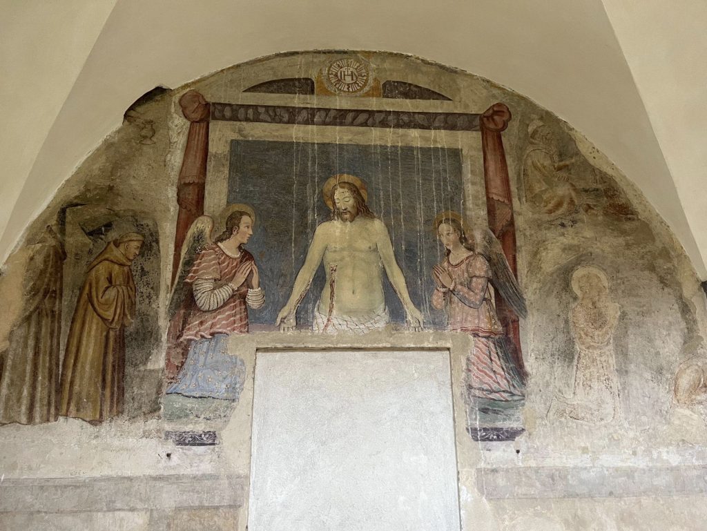 A man with both arms extended before him sits between two angels.