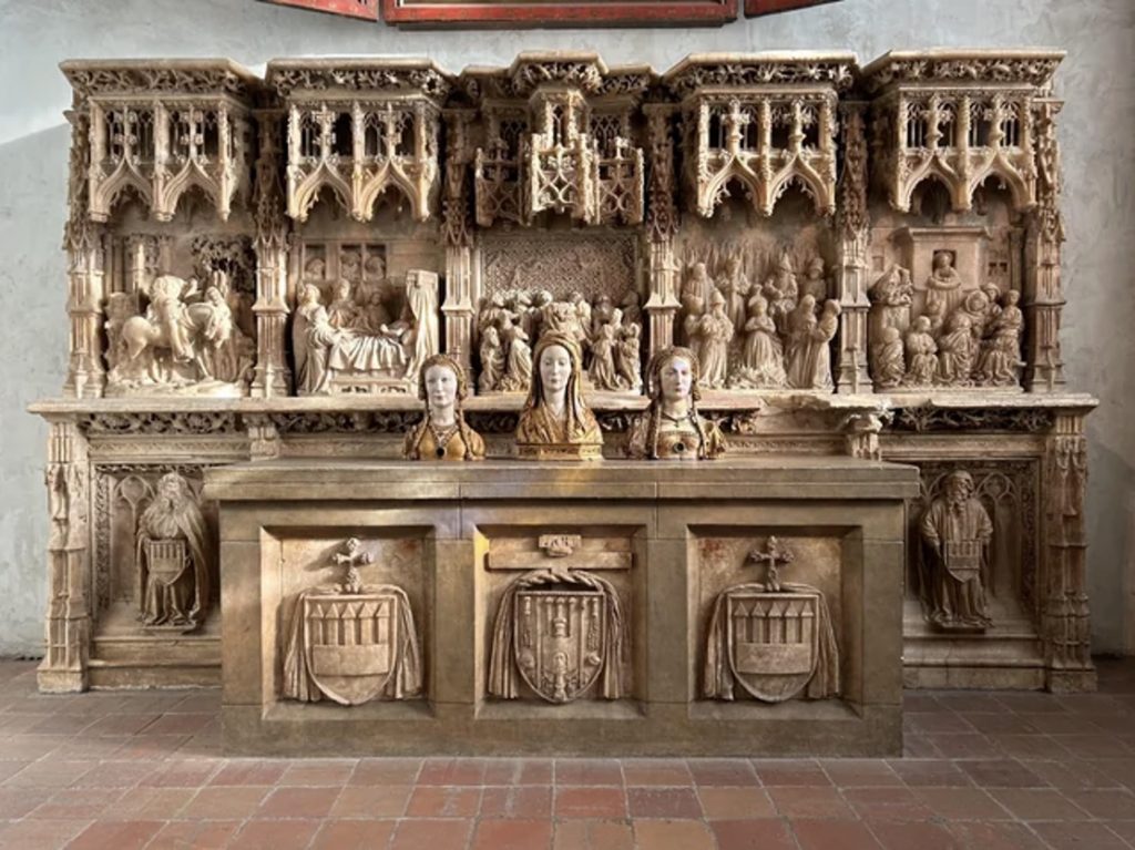 Stone sculpted busts of three women on an altar table with a large stone sculpted screen behind them.
