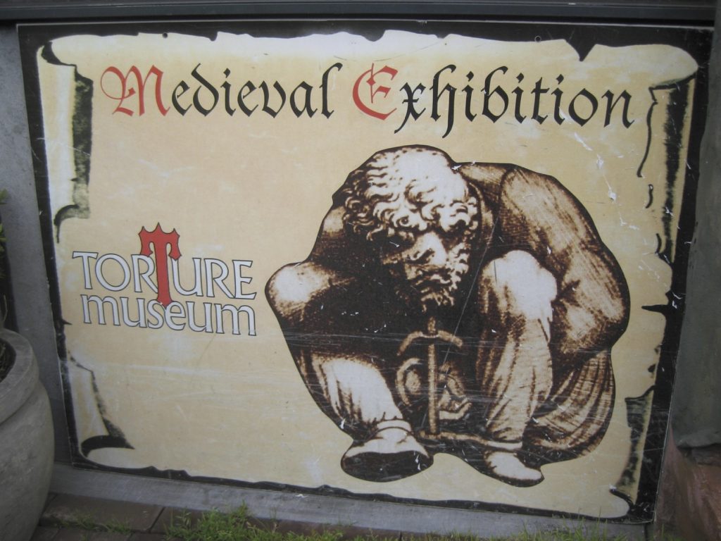 Medieval Torture Museum Sign with a man crouched in chains.