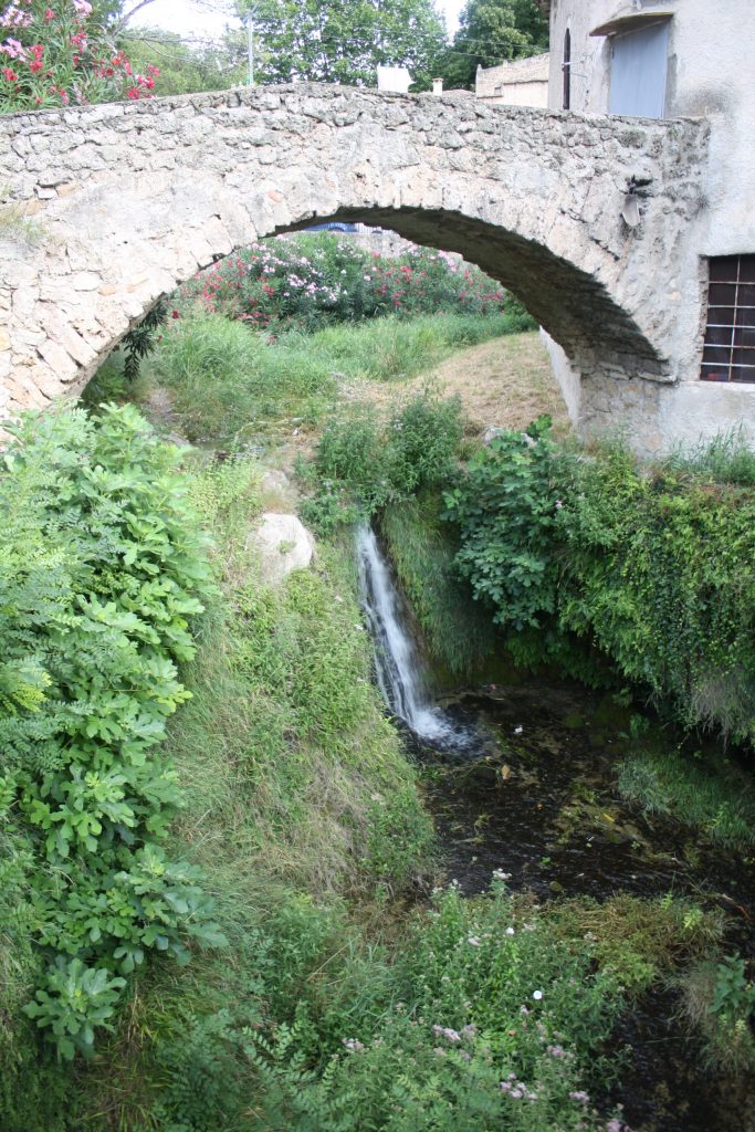 A waterfall flows into a stream over a plant-covered ledge.