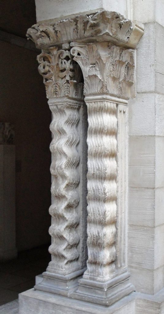 A pair of stone columns carved to resemble rows of waves support capitals and horizontal slabs decorated with leaves.