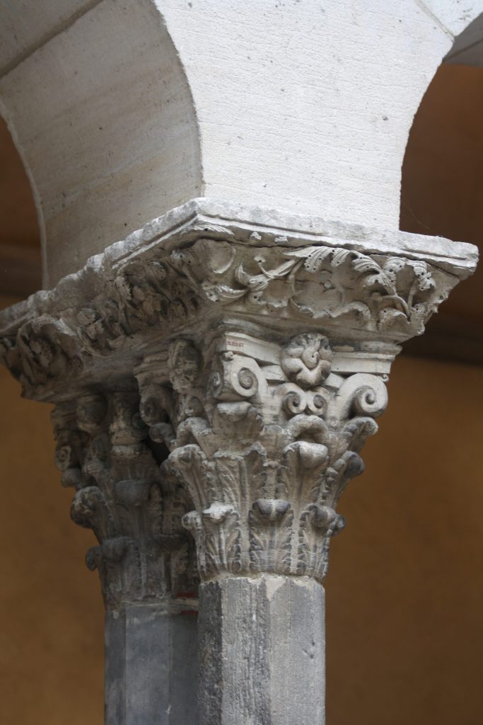 Two identical stone capitals decorated with three tiers of upright leaves that curl forward slightly, surmounted by volutes at the corners and rosettes in between the volutes.