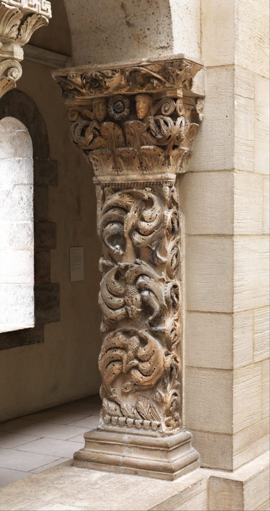 A vertical stone slab placed against the wall, carved with three circular clusters of leaves.