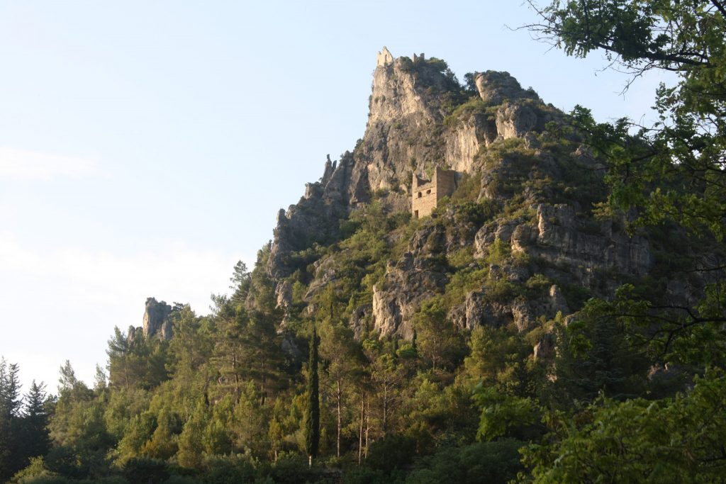 A tall, rocky cliff with a castle built on a ledge in the early evening sunlight.