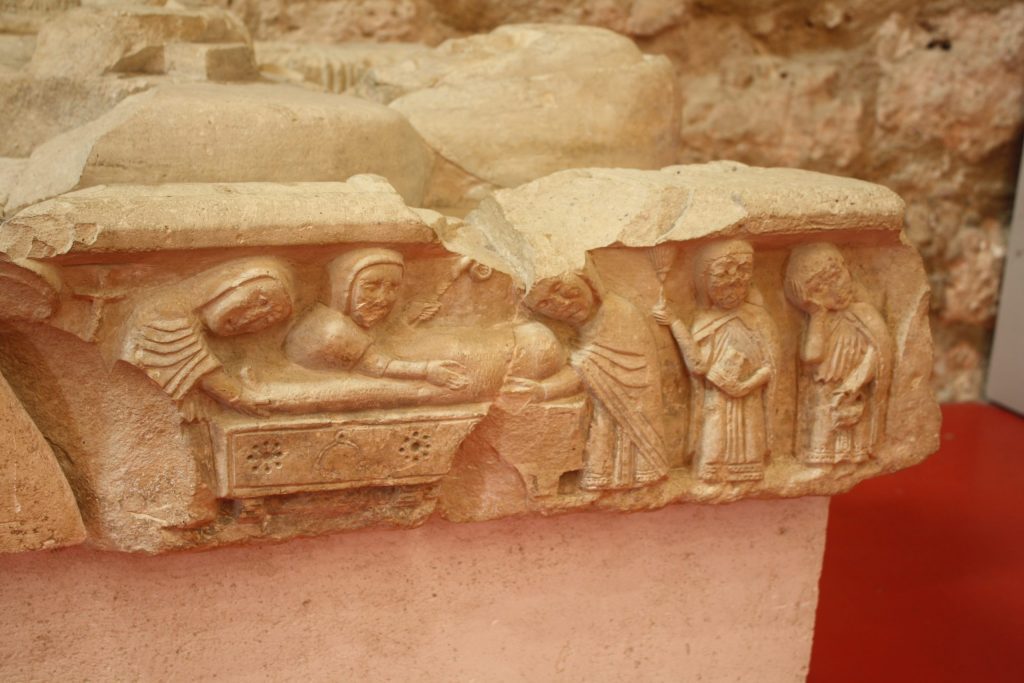 A stone relief sculpture showing a funeral; a body is placed in a tomb by three men while two others mourn.