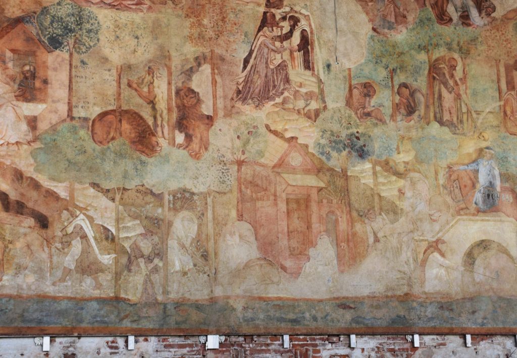 Part of a wall painting with many figures in a complicated landscape that includes a river painted blue along the bottom and trees with green foliage.