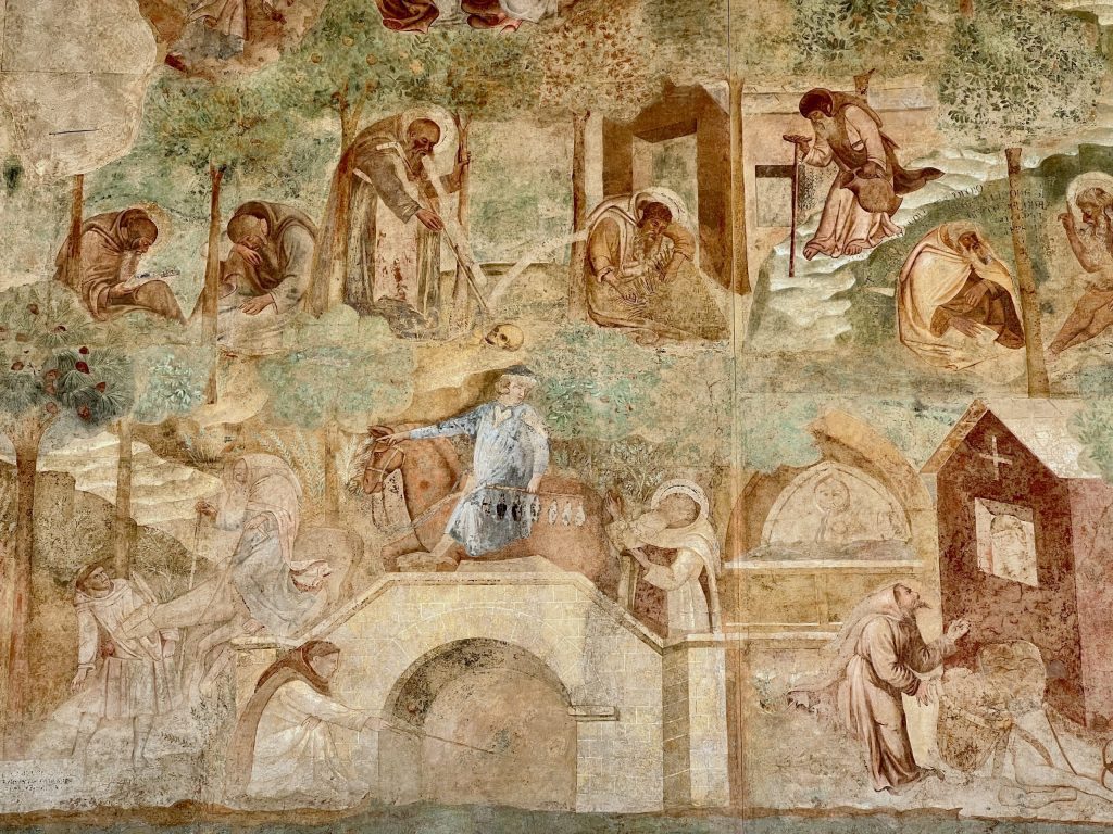 Detail of the Thebaid fresco with numerous hermits and saints, including two scenes from the legend of St Macarius of Egypt. Above, he is talking to a skull, and below, to the devil, who is disguised as a potion salesman, on horseback, crossing a bridge by a river.