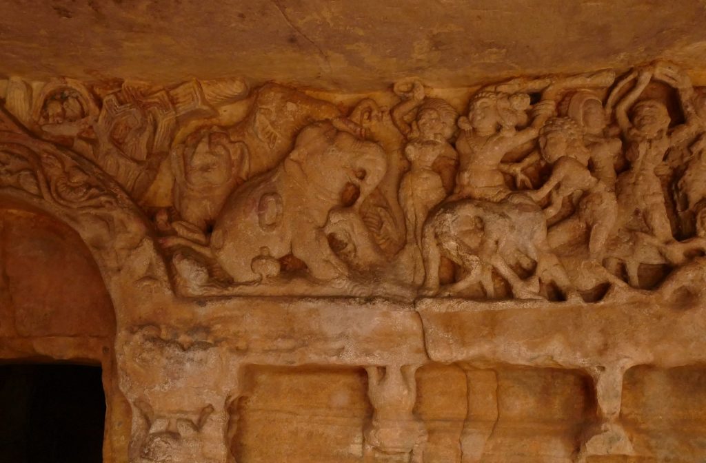Stone relief with herd of elephants and group of humans. The humans gesture wildly and throw objects at the agitated elephants. Udayagiri, Bhubaneswar, Odisha.