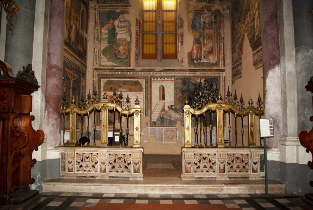 Looking from the nave of San Domenico Maggiore in Naples into a gated chapel covered with frescoes on three walls; the wall on the right features three scenes of the life of the Magdalen.