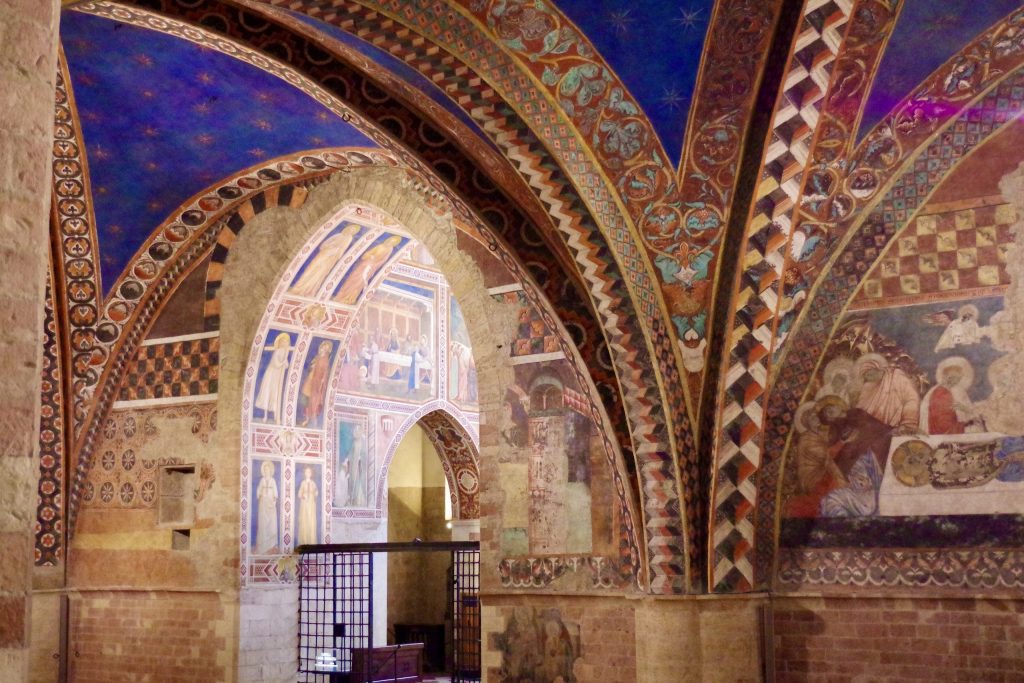 Looking from the nave of the Lower Basilica of St. Francis in Assisi into the Magdalen Chapel, a gated chapel covered with frescoes depicting the life of the Magdalen on three walls.