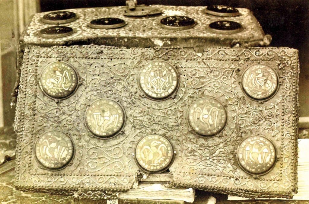 Black and white photograph of a metal box with elaborate swirling vines and enamel metal circles on its top.