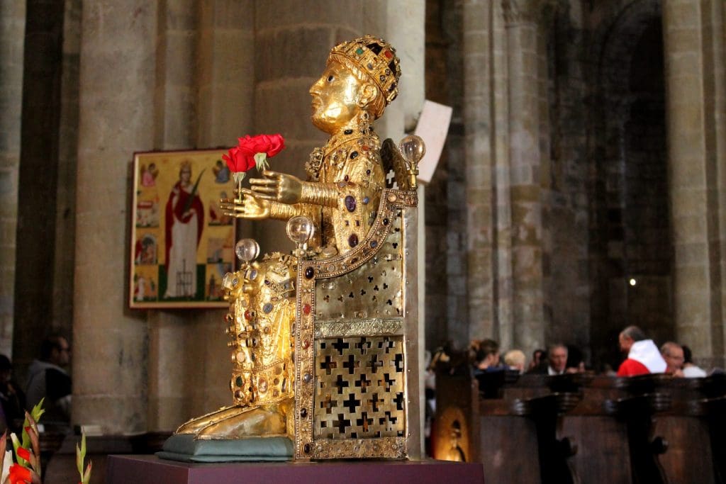 Small sculpture of a young girl sitting on a throne made of gold and encrusted with gems and clear, crystal orbs.