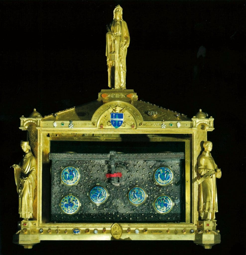 Color photograph of a small metal box decorated with colorful enameled circles resting within a large golden shrine with two figures on the left and right and one tall figure standing on top of the shrine.