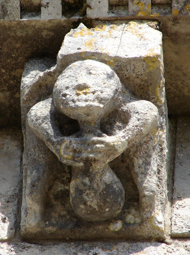 Grimacing corbel figure squats, holds a money bag where his testicles should be.