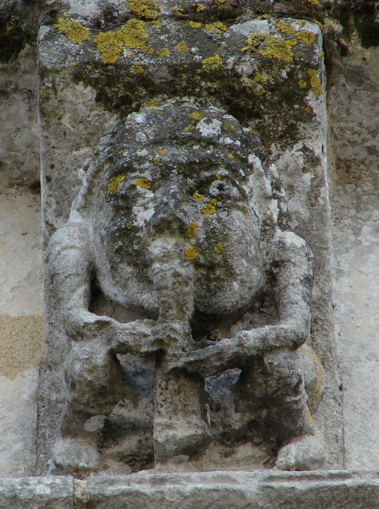 A crouching figure playing a flute that extends from between his legs.