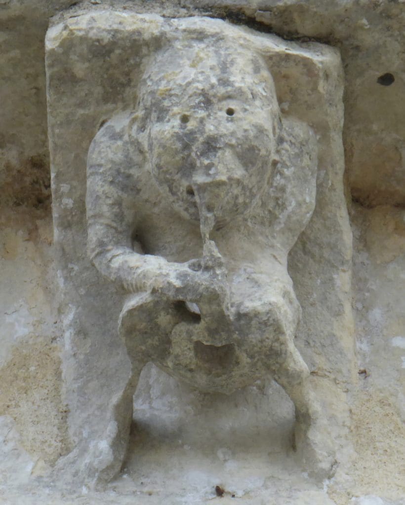 A crouching corbel figure playing a flute that extends from between his legs.