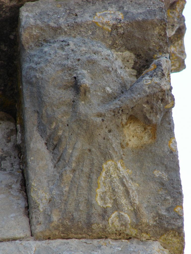 A bearded corbel figure blows a horn to the side and off the edge of a building.
