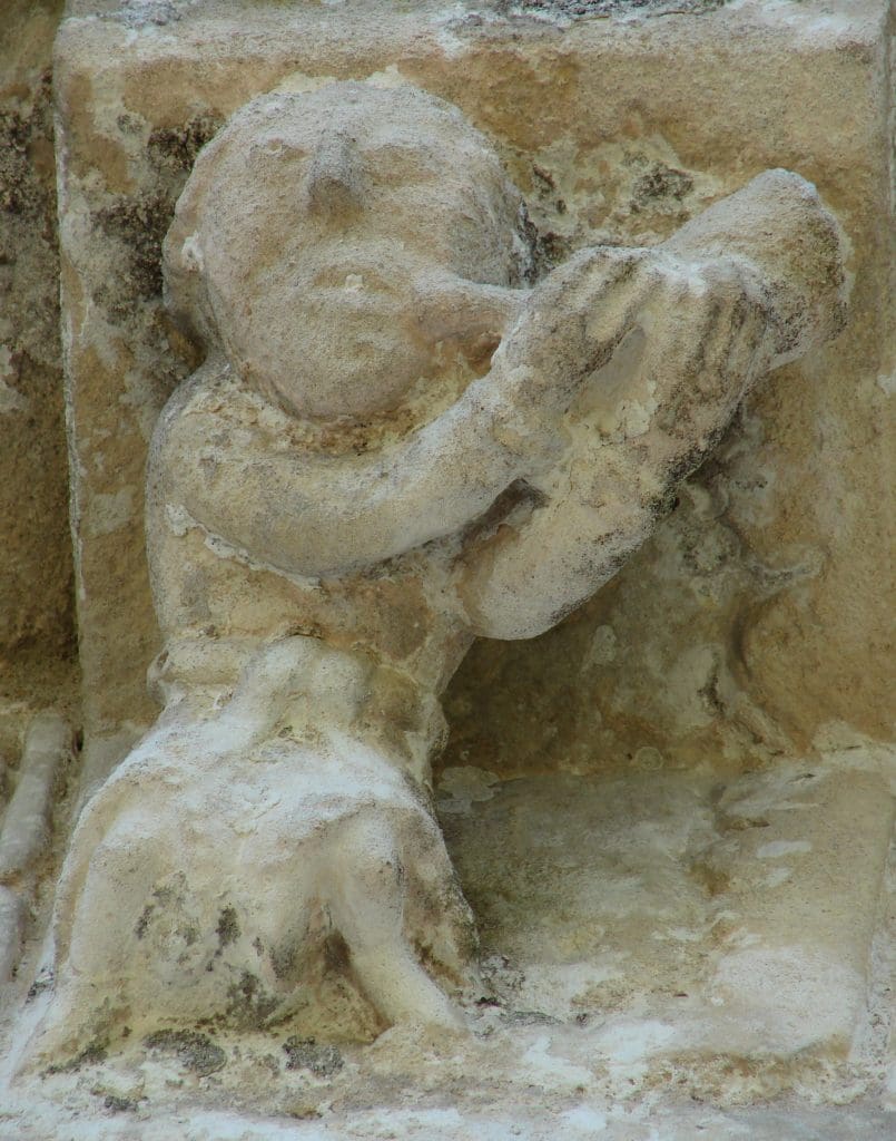Robed corbel figure playing the horn, with a view up his robes.