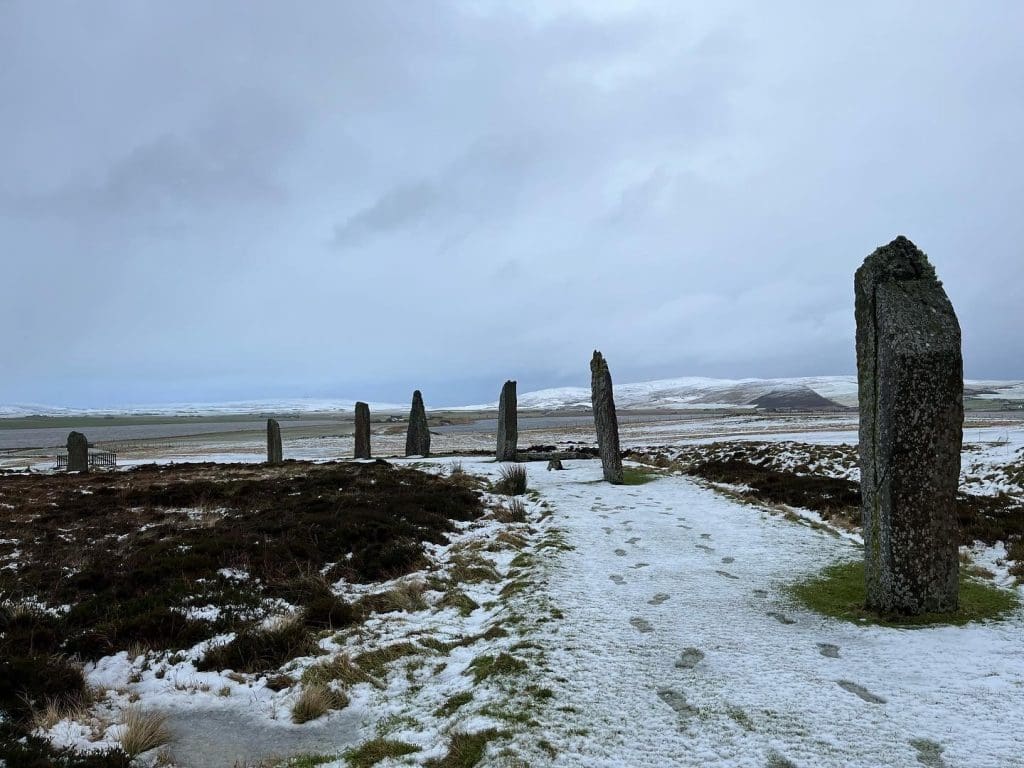 A snowy landscape with a circle of standing stones. Footprints can be seen in the snow.