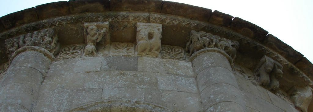 A section of highly ornamented corbel table featuring a horn player, a pair of beasts, an animal with a phallic tail, and a capital with a double-tailed siren.