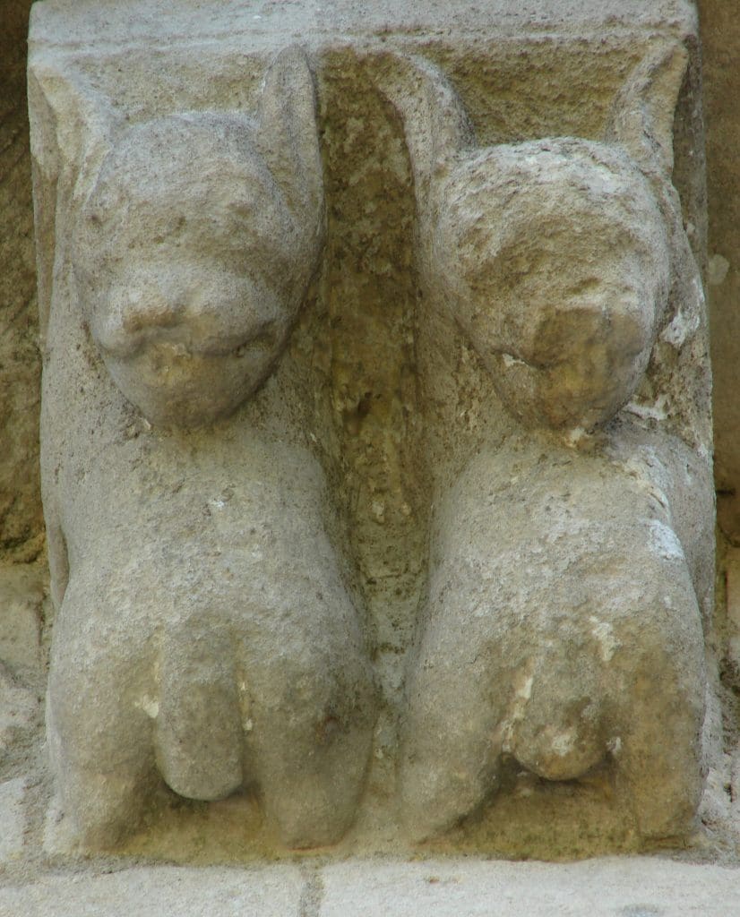 Two male dog-like corbel creatures look backwards over their own bodies