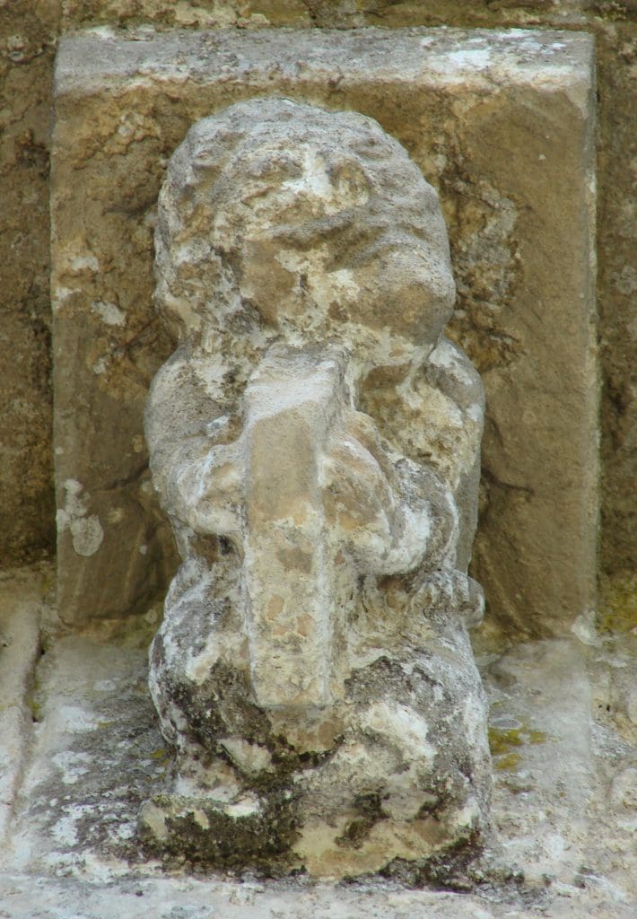 A corbel figure with a moustache plays a harp that extends from between his legs.