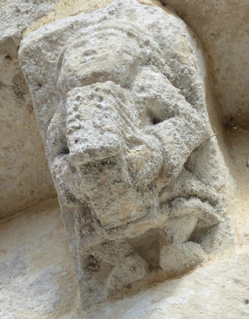 A robed corbel figure plays a harp that extends from between his legs.