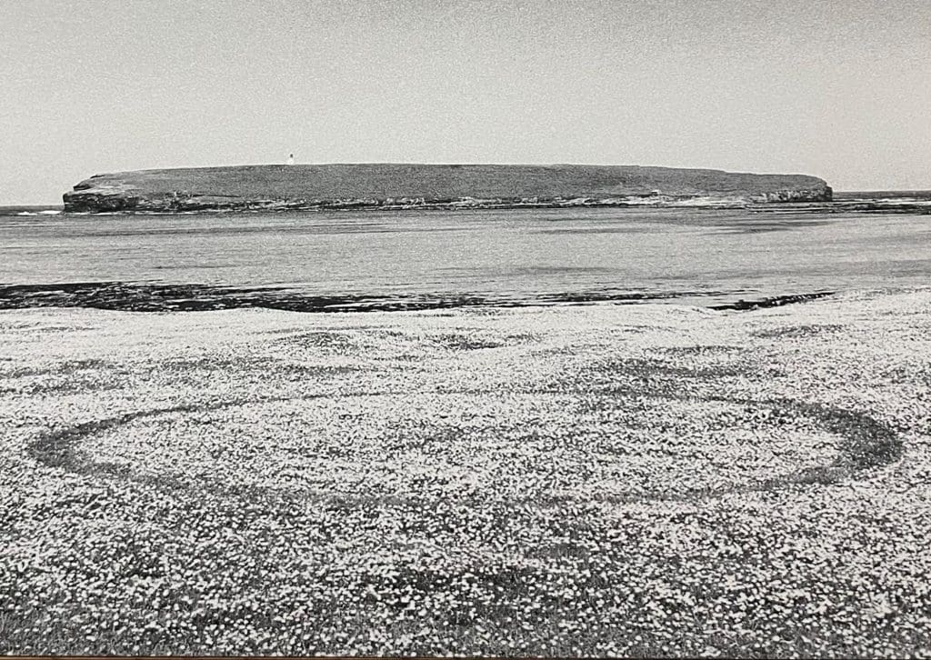 A black and white landscape photo of a tidal island, with a circular path in the foreground.