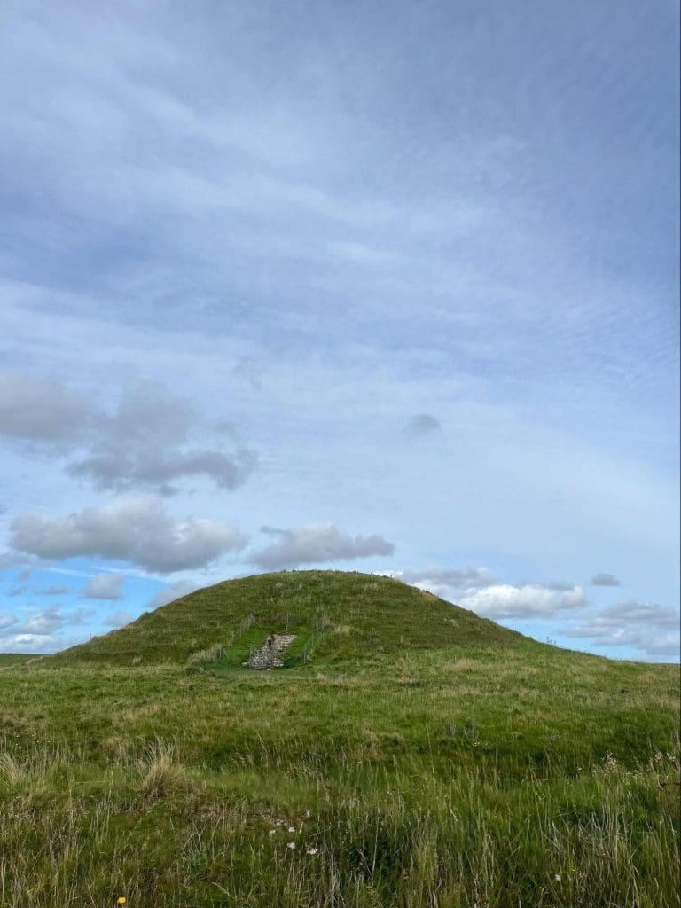 A grassy green burial mound in a field.