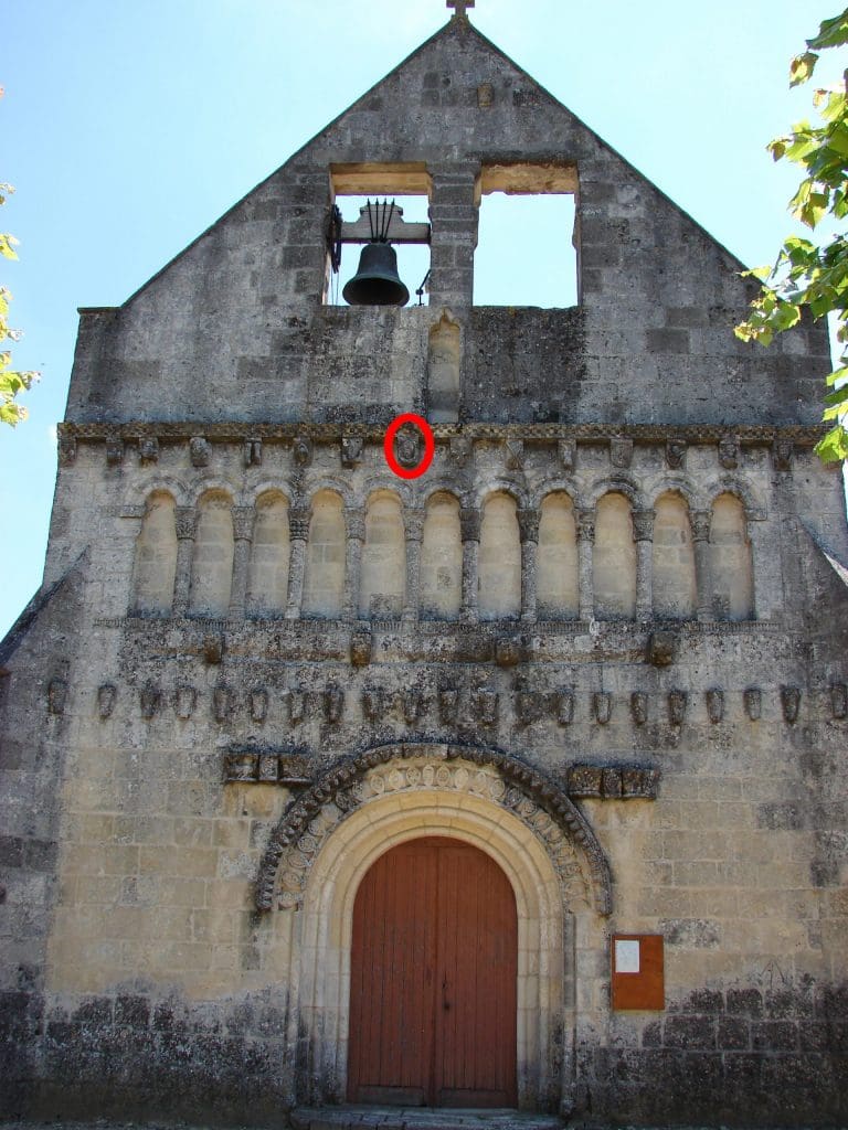 Screen facade of small Romanesque church with sparse sculpture and a bell at top.