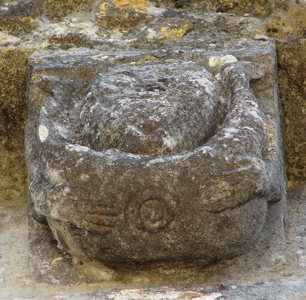 Corbel figure with feet around ears, exposing anus, different view.