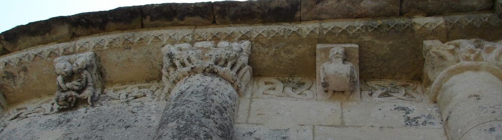 Section of a highly ornamented corbel table featuring quatrefoil metopes and corbels with a fornicating couple and a man with a barrel.