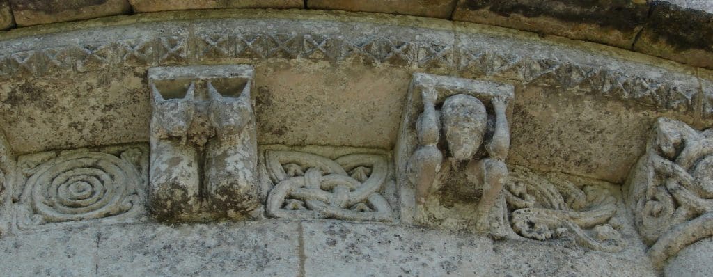 Section of a highly ornamented corbel table featuring quatrefoil metopes and corbels with a pair of male oxen and a squatting man holding up the roof.