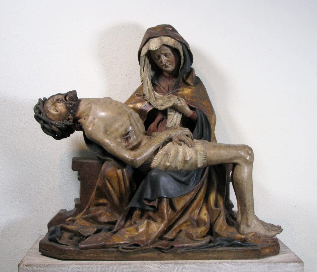 A sculpture depicting the Virgin Mary in voluminous robes holding the dead Christ, shown with prominent ribs and head falling backward.