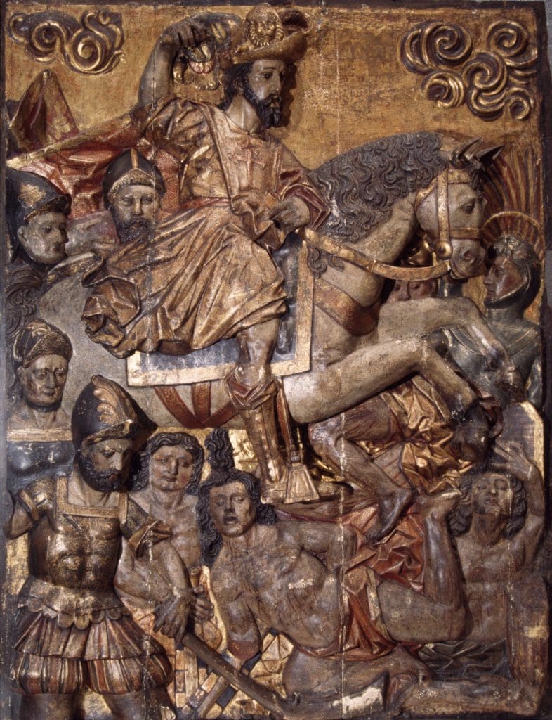 Polychrome wood carving of a knight on horseback surrounded by knights to the left and trampling dismembered bodies with gold leaf covering the background and knight’s costumes.