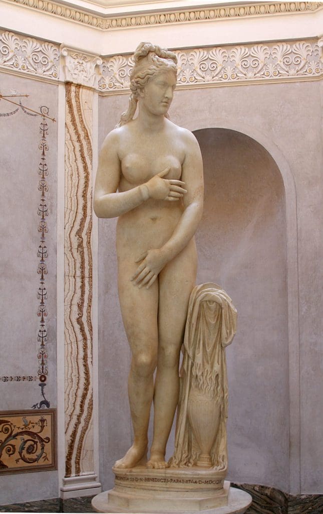 Fig. 4: A life-sized marble sculpture of a standing nude woman. Standing contrapposto with her weight on her left leg, she turns her head to her left. Her left hand is held in front of her while her right is held across her body below her chest.