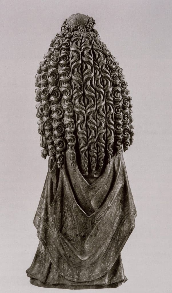 Photograph of a sculpture of a standing woman with very long, elaborately carved wavy hair flowing down her back.