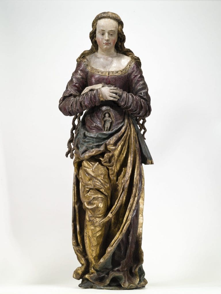 Photograph of a sculpture of an elaborately dressed pregnant woman. The baby is visible in an oval abdominal opening.